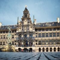 The City Hall (Dutch: Stadhuis) of Antwerp, Belgium, stands on the western side of Antwerp's Grote Markt (Great Market Square). Erected between 1561 and 1565 after designs made by Cornelis Floris de Vriendt and several other architects and artists, this Renaissance building incorporates both Flemish and Italian influences. The City Hall is inscribed on UNESCO's World Heritage List along with the belfries of Belgium and France. Margaret of Parma hands over the keys to the city, by Henri Leys In the 16th century Antwerp became one of the busiest trading ports and most prosperous cities in Northern Europe. The municipal authorities wished to replace Antwerp's small medieval town hall with a more imposing structure befitting the prosperity of the great port city. Antwerp architect Domien de Waghemakere drafted a plan (c. 1540) for a new building in a style typical of the monumental Gothic town halls of Flanders and Brabant. But the threat of war prevented any progress on the project. The building materiasl intended for the city hall were instead used to shore up the city defenses. Not until about 1560 new plans were developed. In the meantime Gothic architecture had gone out of fashion. The new designs for the city hall were in the new Renaissance style. Completed in 1565, the building lasted hardly a decade before being burnt to a shell in the Spanish Fury of 1576. It was restored three years later. The low arcaded ground story is of rusticated stone, and at one time housed little shops. Above are two stories with Doric and Ionic columns separating large mullioned windows, and a fourth story forming an open gallery. The richly ornamented central section, which rises above the eaves in diminishing stages, holds female statues representing Justice, Prudence, and the Virgin Mary, and bears the coats of arms of the Duchy of Brabant, the Spanish Habsburgs, and the Margraviate of Antwerp. Renovations during the late 19th century by architects Pierre Bruno Bourla, Joseph