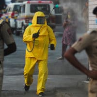 A civic worker sanitizes an area as policemen stand guard after a protest against the extension of the lockdown, at a slum in Mumbai, India, April 14, 2020. Rafiq Maqbool | AP