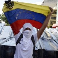 VENEZUELA-OPPOSITION-DEMO A demonstrator holds a Venezuelan flag in front of riot policemen during an opposition demo against the government of Venezuelan President Nicolas Maduro, in Caracas on February 12, 2014. Unidentified assailants on a motorcycle fired into a crowd of anti-government protesters, wounding at least two people. AFP PHOTO / JUAN BARRETO