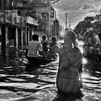 Shahidul Alam/Drik/Majority World (Bangladesh), The resilience of the average Bangladeshi is remarkable. As this woman waded through the flood waters in Kamalapur to get to work, there was a photographic studio ‘Dreamland Photographers’, which was open for business, 1988.