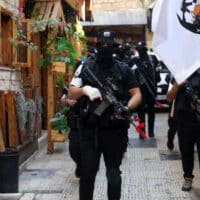 MEMBERS OF THE LIONS’ DEN HOLD THEIR WEAPONS NEXT TO A FLAG FLYING THE LIONS’ DEN LOGO DURING A MEMORIAL SERVICE OF MOHAMMED AL-AZIZI AND ABDUL RAHMAN SOBH WHO WERE KILLED BY ISRAELI FORCES, IN THE WEST BANK CITY OF NABLUS ON SEPTEMBER 2, 2022. (PHOTO: SHADI JARAR’AH/ APA IMAGES)